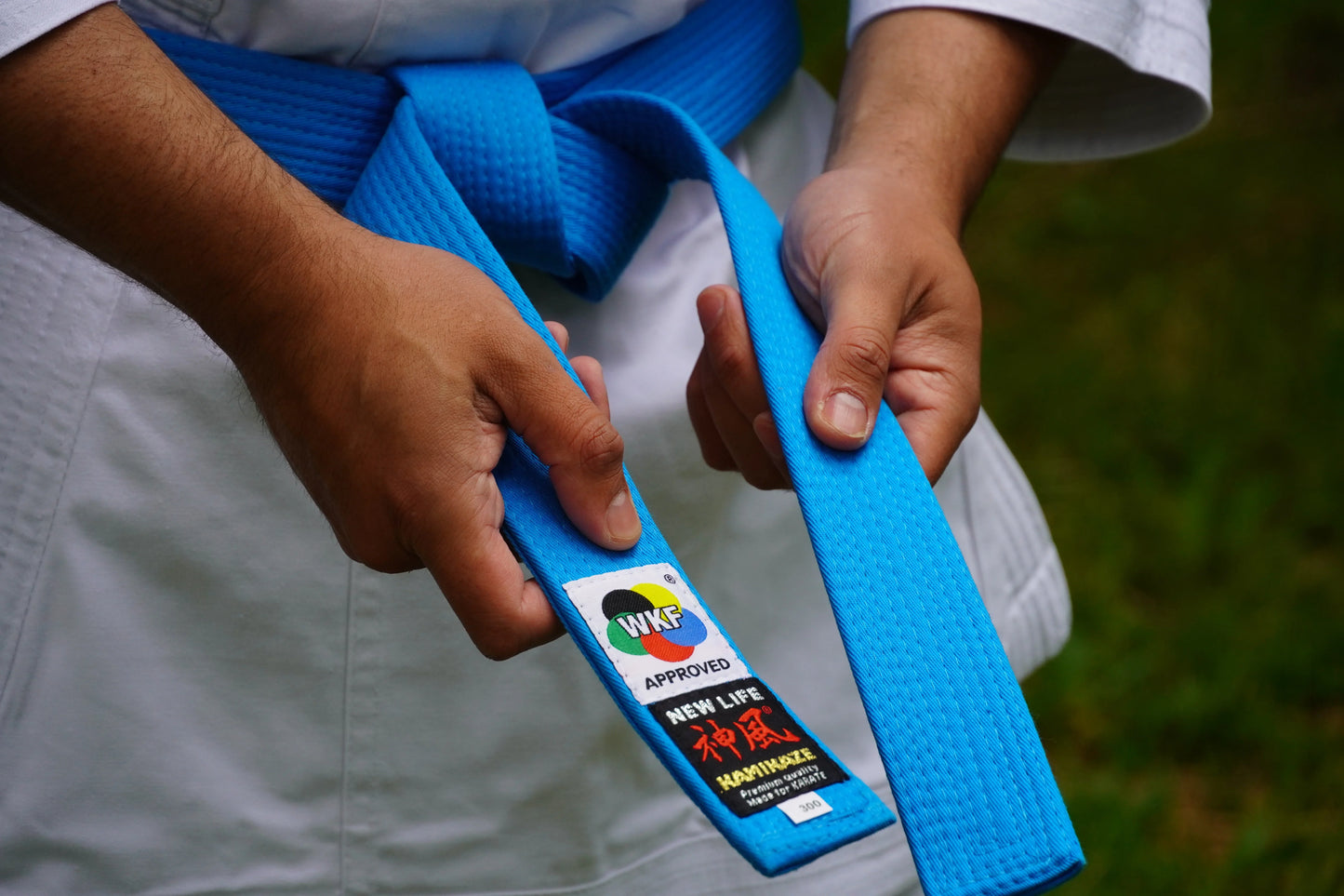 Person in karate gi tying blue karate belt with WKF approved tag outdoors